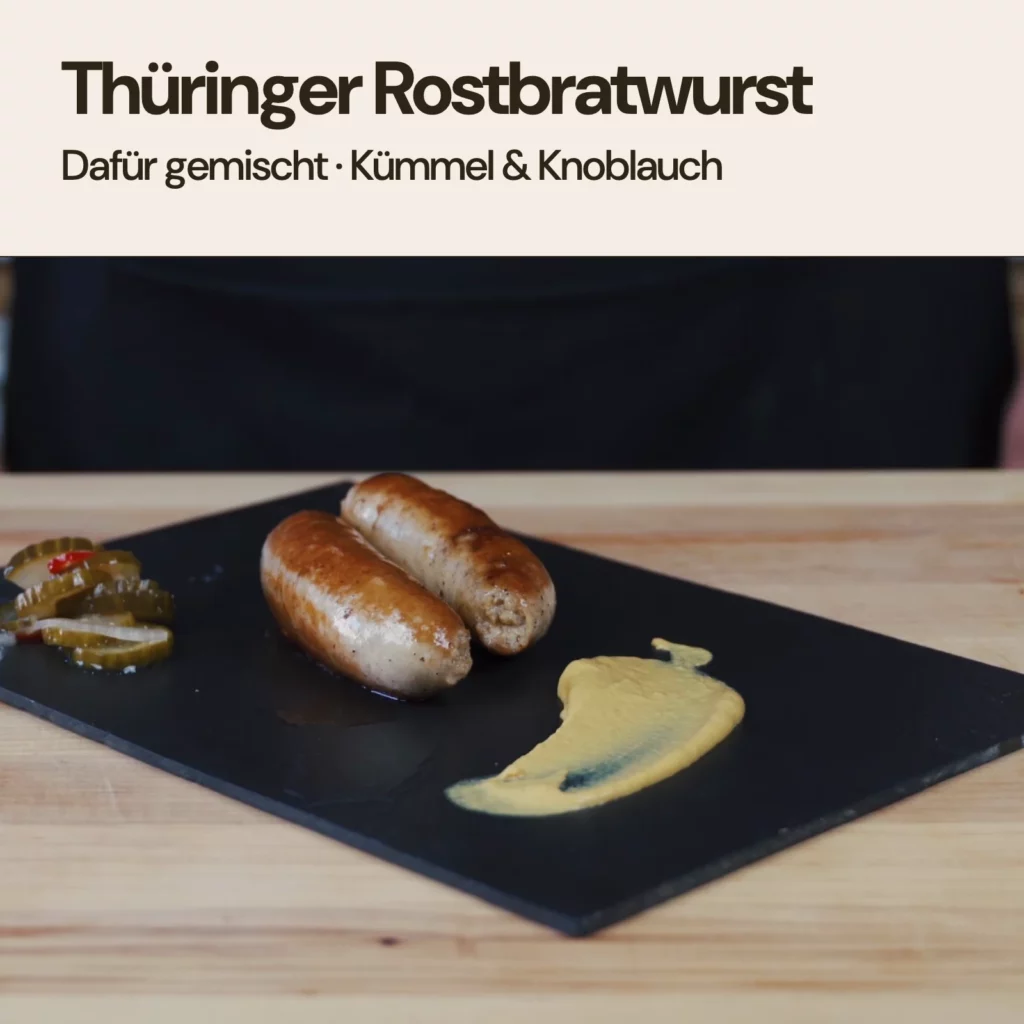 Zwei gebratene Thüringer Rostbratwürste mit Senf und Gurken auf einer Schieferplatte. thüringer art ist die Mischung für Thüringer Rostbratwurst.